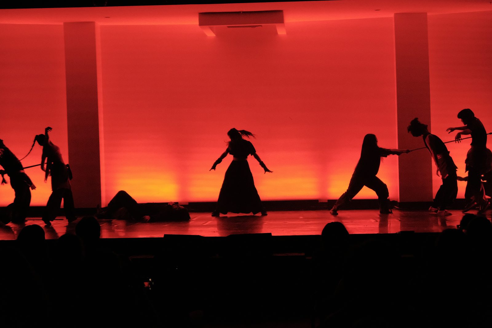 Performers silhouetted in fighting stances against a deep red and orange backlit stage