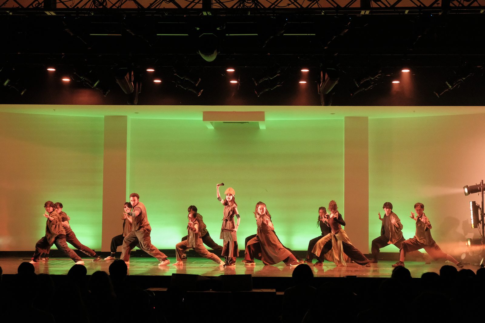 The whole group holding low stances across a green-lit stage