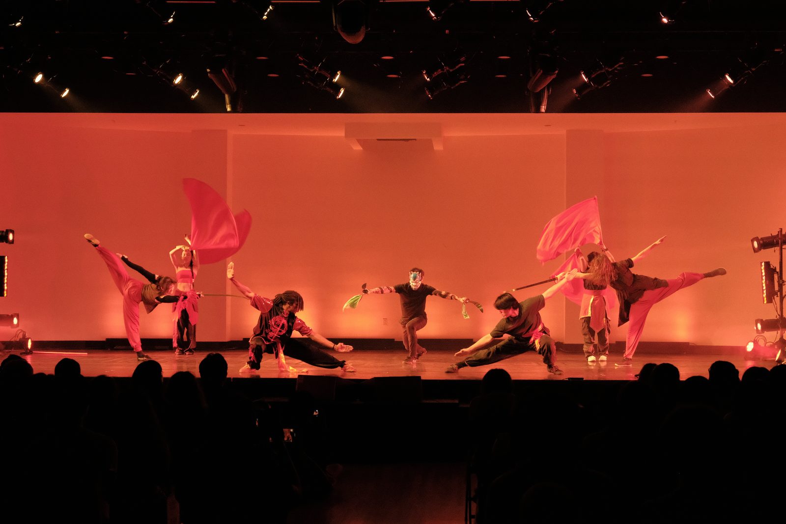 Performers sweeping large red fans through the air on an orange-lit stage