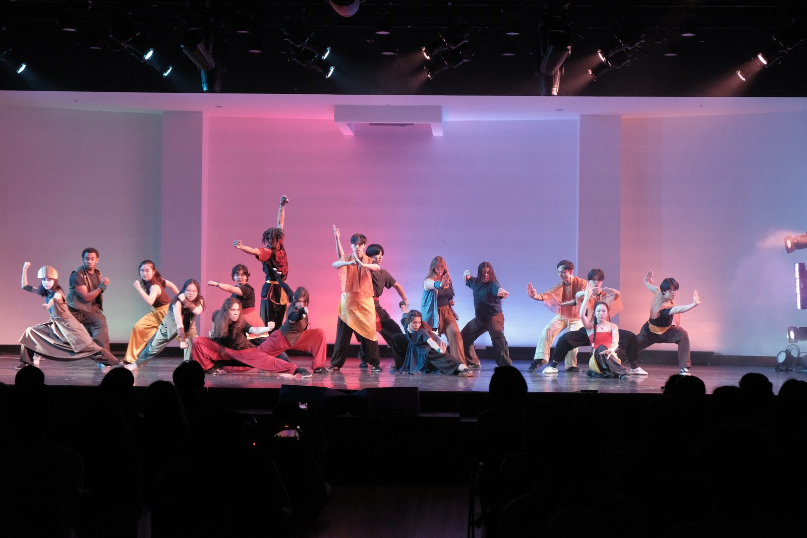 A large group formation in varied stances under pink and purple stage lighting