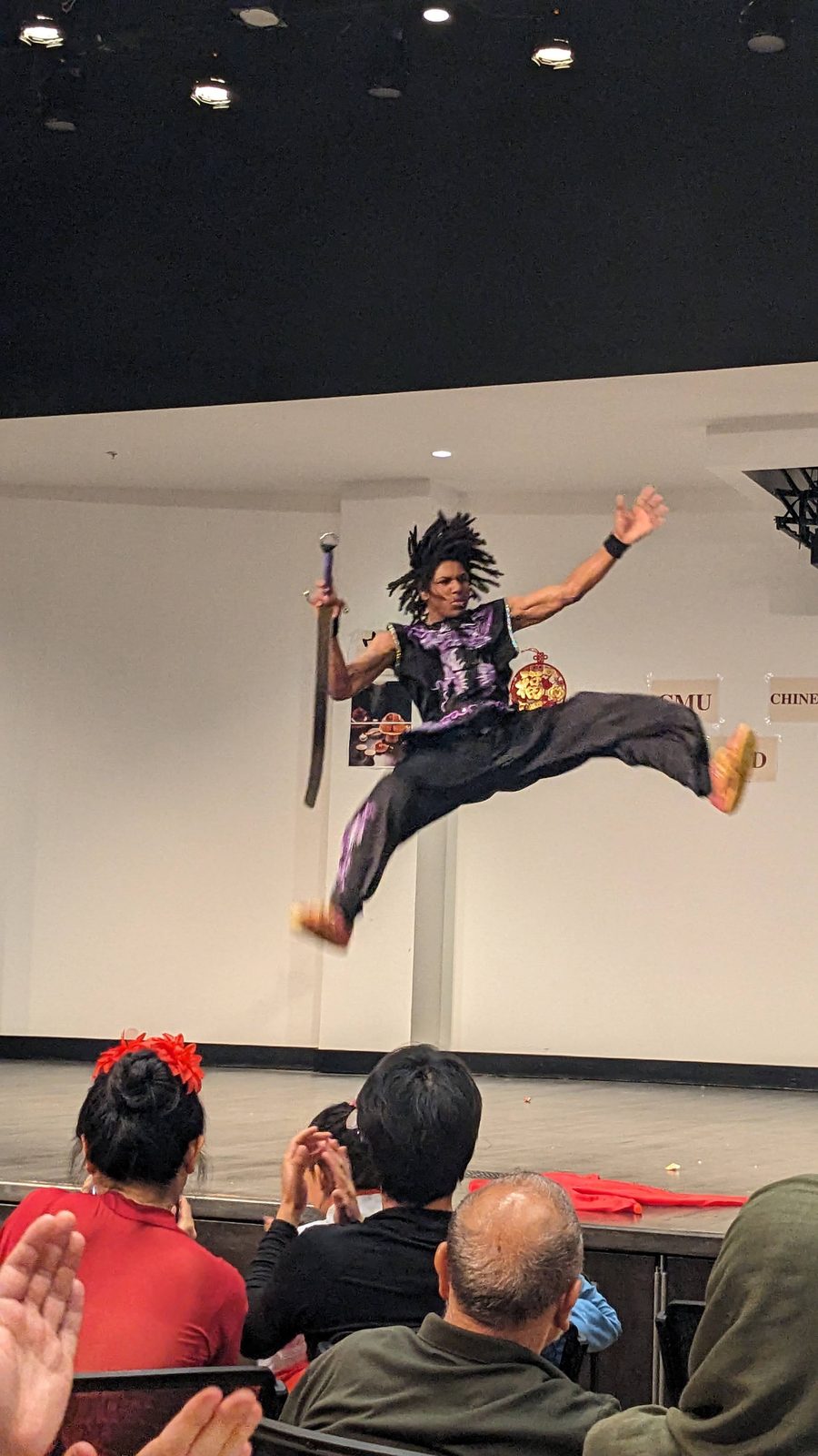 A performer leaping high with a weapon while the audience watches from the foreground