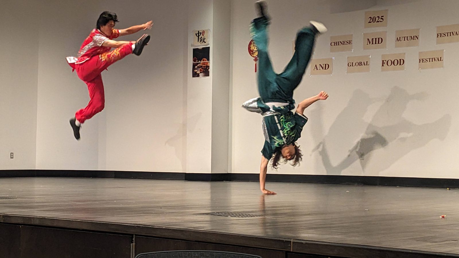 Two performers airborne at the same moment, one in a jump kick and one inverted mid-aerial