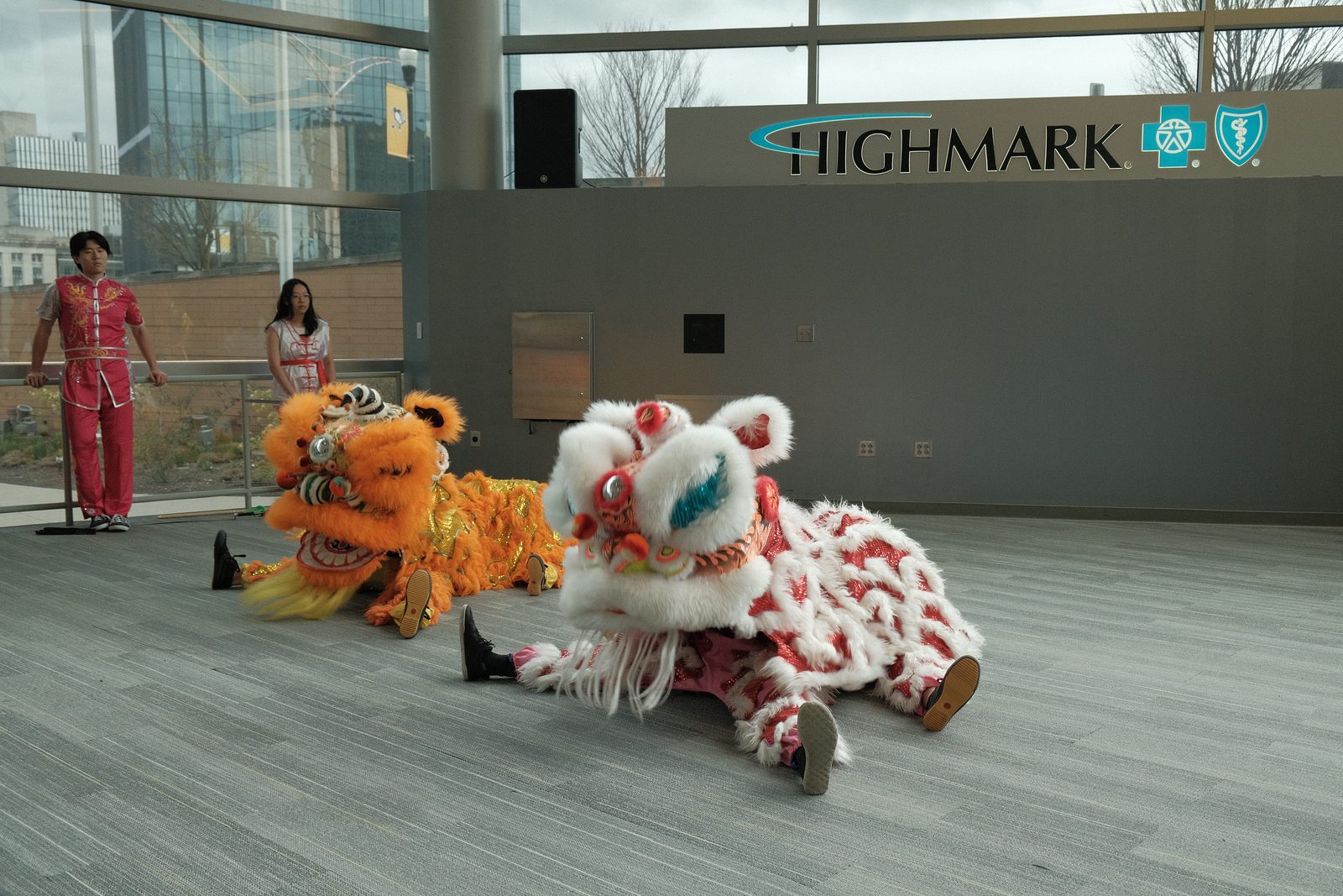 Two lion dance costumes, one orange and one white and red, performing on the arena concourse