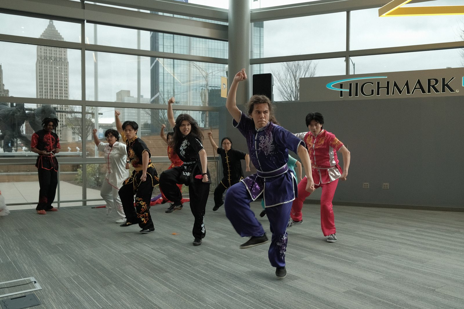 Club members performing a group routine in front of the arena windows, one leaping with an arm raised