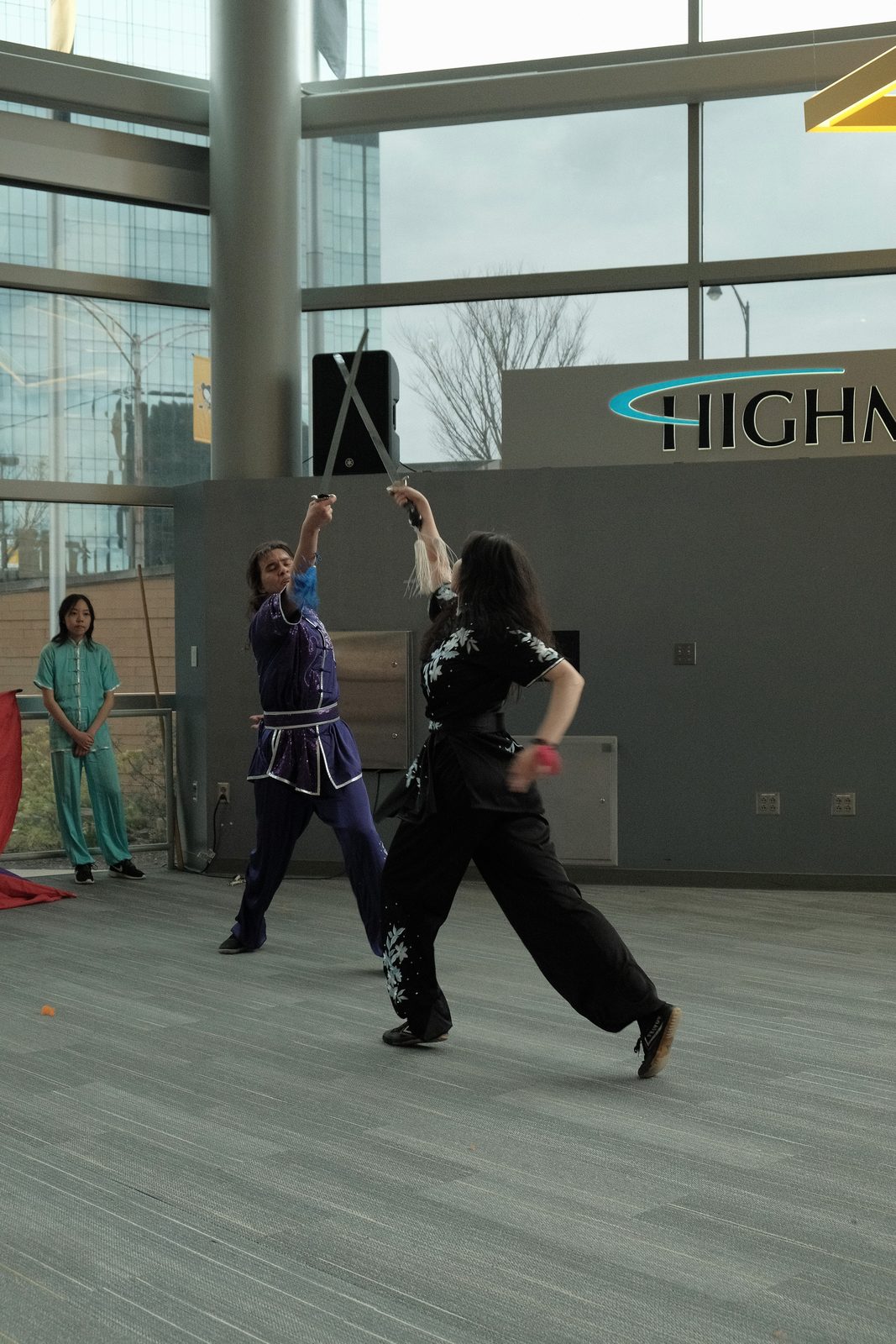 A performer raising a weapon overhead mid-form while another moves alongside