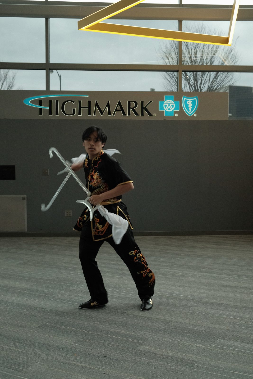A performer in a black uniform mid straightsword form, the white tassel trailing behind the blade
