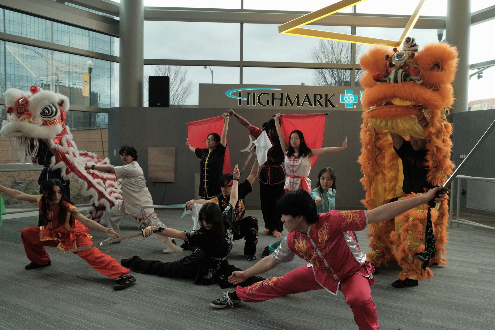 The full group in a finale pose with two lion dance costumes and red flags raised